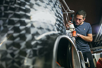 Ein junger Mann steht an einem Stahltank im Weinkeller. © Hessen schafft Wissen – Steffen Böttcher