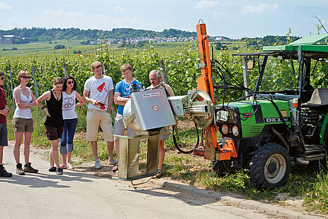 Eine Gruppe von Studierenden steht mit einem Dozenten neben einem Traktor im Weinberg © Hochschule Geisenheim / ppsstudios.com