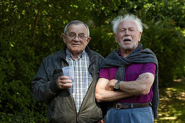 Zwei Männer stehen vor grüner Hecke