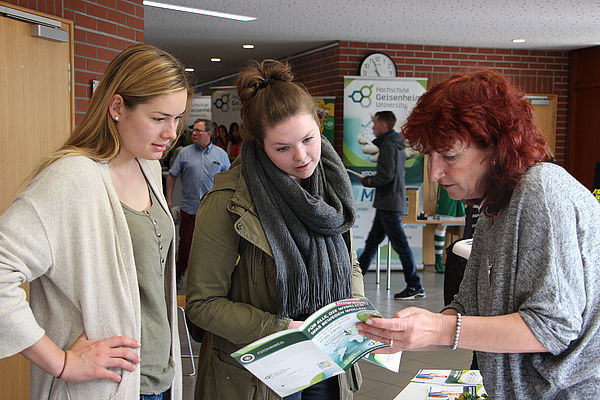 Eine Frau erklärt zwei jungen Mädchen etwas anhand einer Broschüre. © Hochschule Geisenheim