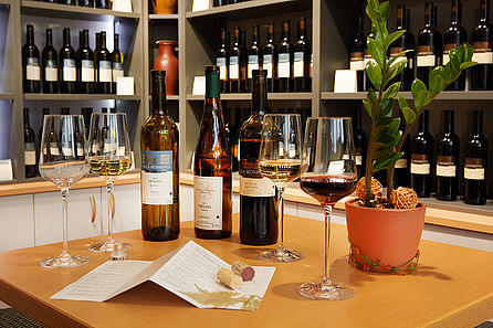 Mehrere geöffnete Flaschen Wein stehen mit Gläsern auf einem Tisch. Im Hintergrund sind Weinregale zu sehen. © Hochschule Geisenheim / Winfried Schönbach