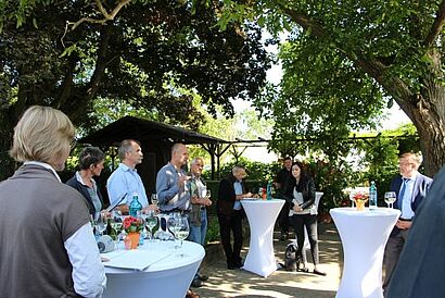 Teilnehmer draussen unter Bäumen an weissen Stehtischen