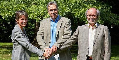 Frontalaufnahme von neuer Vizepräsidentin und zwei Professoren, die lächelnd die Hände übereinander legen 