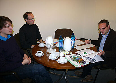 Männer sitzen an einem  Holztisch 