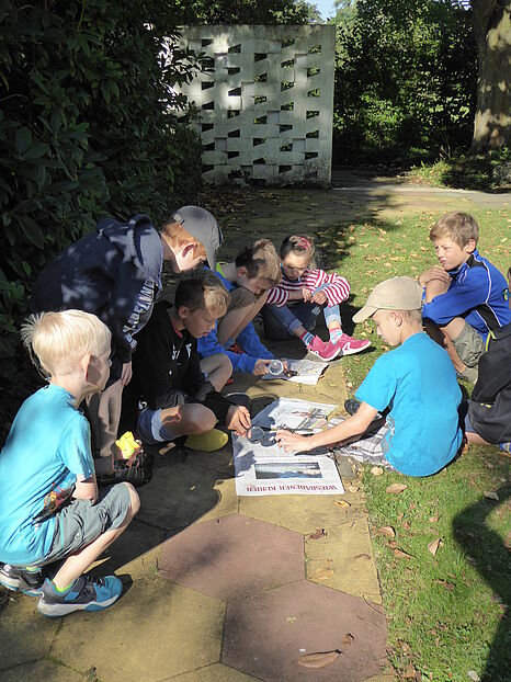 [Translate to English:] Kinder untersuchen eine Zeitung mit einer Lupe