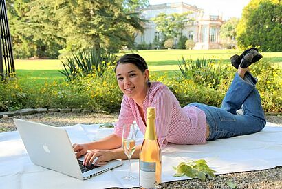 Studentin liegt auf einer Picknickdecke mit ihrem Laptop