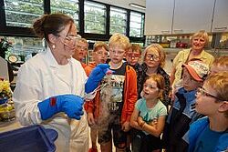 Forscherin umgeben von Kindern und älterer Dame im Hintergrund