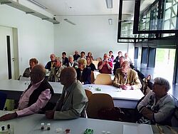 Publikum sitzen an Tischen und hören zu