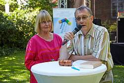 Mann mit Mikrofon am Stehtisch neben ihm steht eine Frau