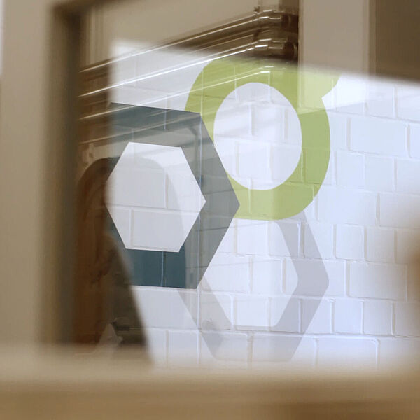 Das Logo der Hochschule Geisenheim ist an eine weiße Steinwand angebracht. © Hochschule Geisenheim