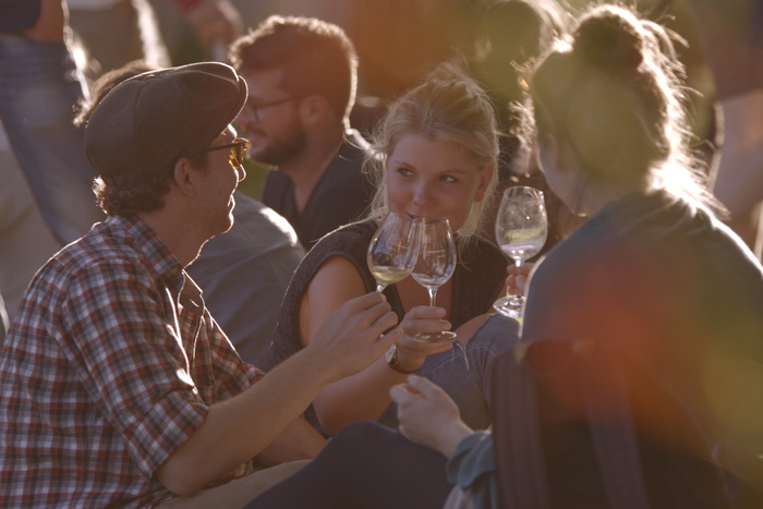 Eine Gruppe junger Menschen sitzt zusammen und stößt mit Wein an. © Hochschschule Geisenheim
