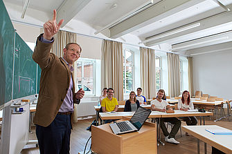 Ein Dozent steht vor einer Gruppe Studierender und erläutert etwas an einer Tafel. © Hochschule Geisenheim / pps-studios.com