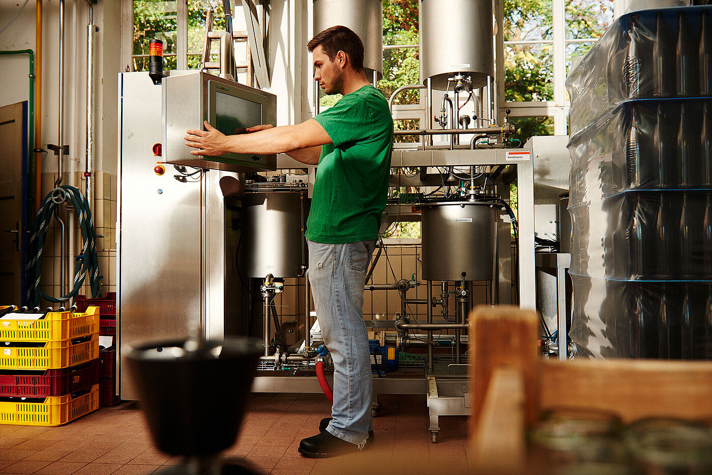 Ein junger Mann steht an einer modernen technischen Anlage. Rechts stehen Paletten mit leeren Flaschen. © Hessen schafft Wissen / Daniel Chassein