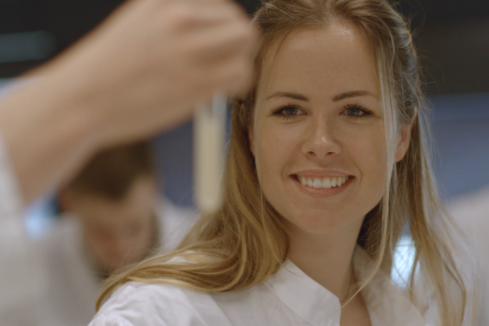 Eine junge Frau im Laborkittel betrachtet den Inhalt eines Reagenzglases. © Hochschschule Geisenheim