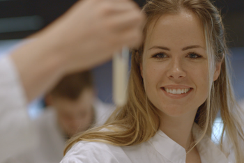 Eine junge Frau im Laborkittel betrachtet den Inhalt eines Reagenzglases. © Hochschschule Geisenheim