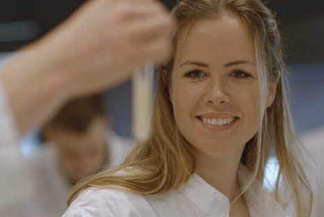 Eine junge Frau im Laborkittel betrachtet den Inhalt eines Reagenzglases. © Hochschschule Geisenheim