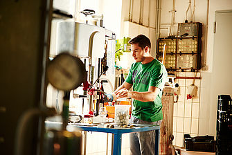 Ein junger Mann steht an einer Anlage, die Flaschen verschließt. © Hessen schafft Wissen / Daniel Chassein