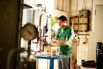 Ein junger Mann steht an einer Anlage, die Flaschen verschließt. © Hessen schafft Wissen / Daniel Chassein