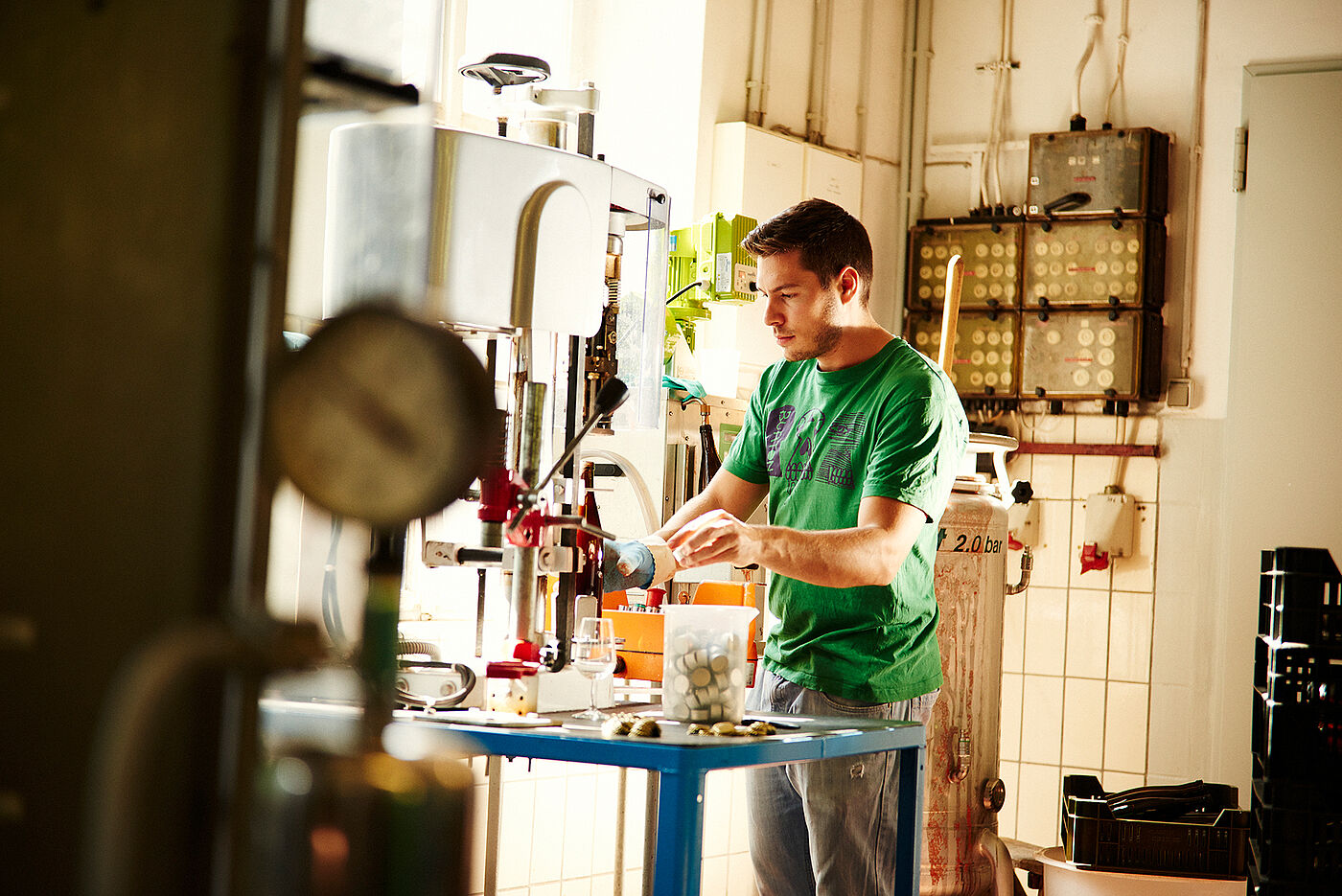 Ein junger Mann steht an einer Anlage, die Flaschen verschließt. © Hessen schafft Wissen / Daniel Chassein