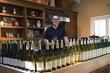 Bas van Gijzen steht im Hintergrund von vielen Weinflaschen