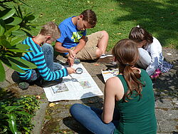 Kinder sitzen draussen am Boden und zeichnen