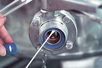 Eine Person macht einen Abstrich am Auslauf eines Stahltanks. © Hochschule Geisenheim / pps-studios.com