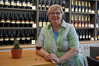 Prof.Dr.Monika Christmann sitzt vor Weinregal 