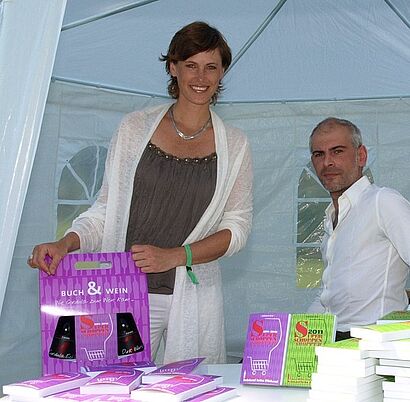 Frau hält Buch&Wein Pack in den Haenden , neben ihr steht ein Mann