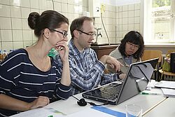 Zwei Frauen und ein Mann sitzen vor einem Laptop