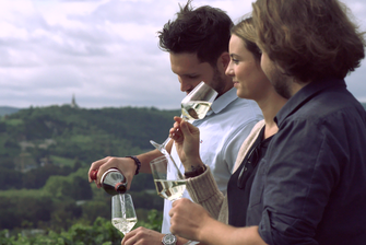 Drei junge Menschen stehen vor einem Weinbergspanorama und trinken Wein. © Hochschschule Geisenheim