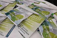 Gummibärchen, Postkarten und Kugelschreiber mit Hochschullogo liegen auf einem Tisch. © Hochschule Geisenheim