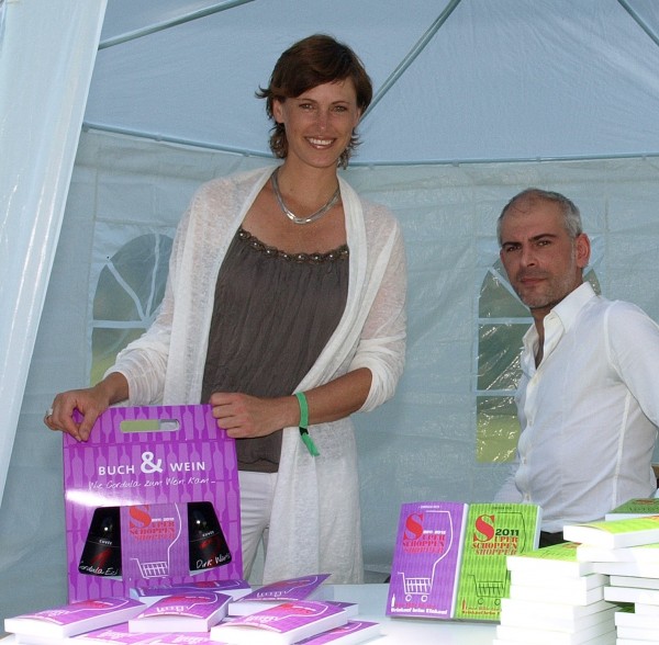 Frau hält Buch&Wein Pack in den Haenden , neben ihr steht ein Mann